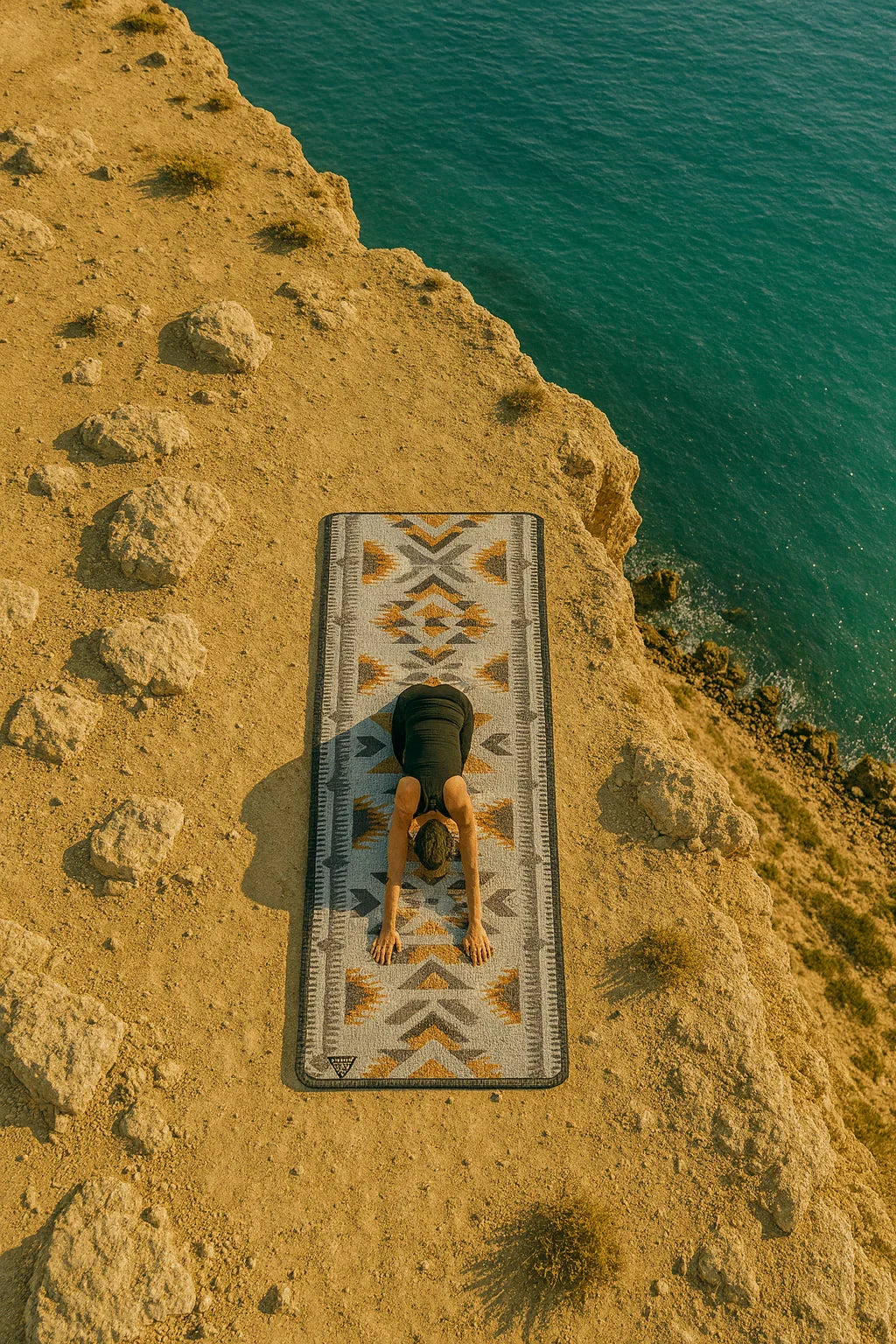 Person lying on a patterned mat by a body of water