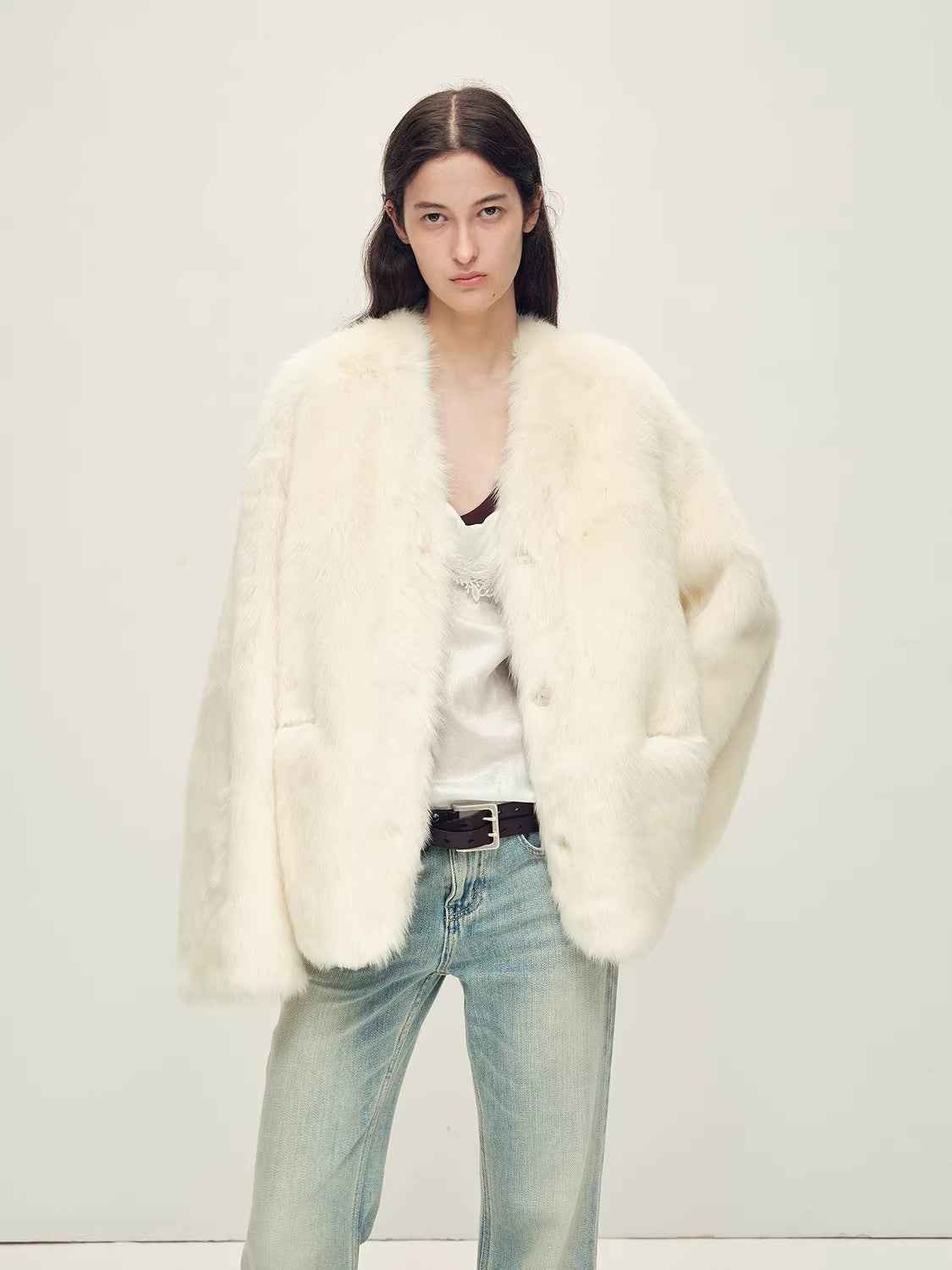 Person wearing a white fur coat, white top, and light blue jeans on a plain background