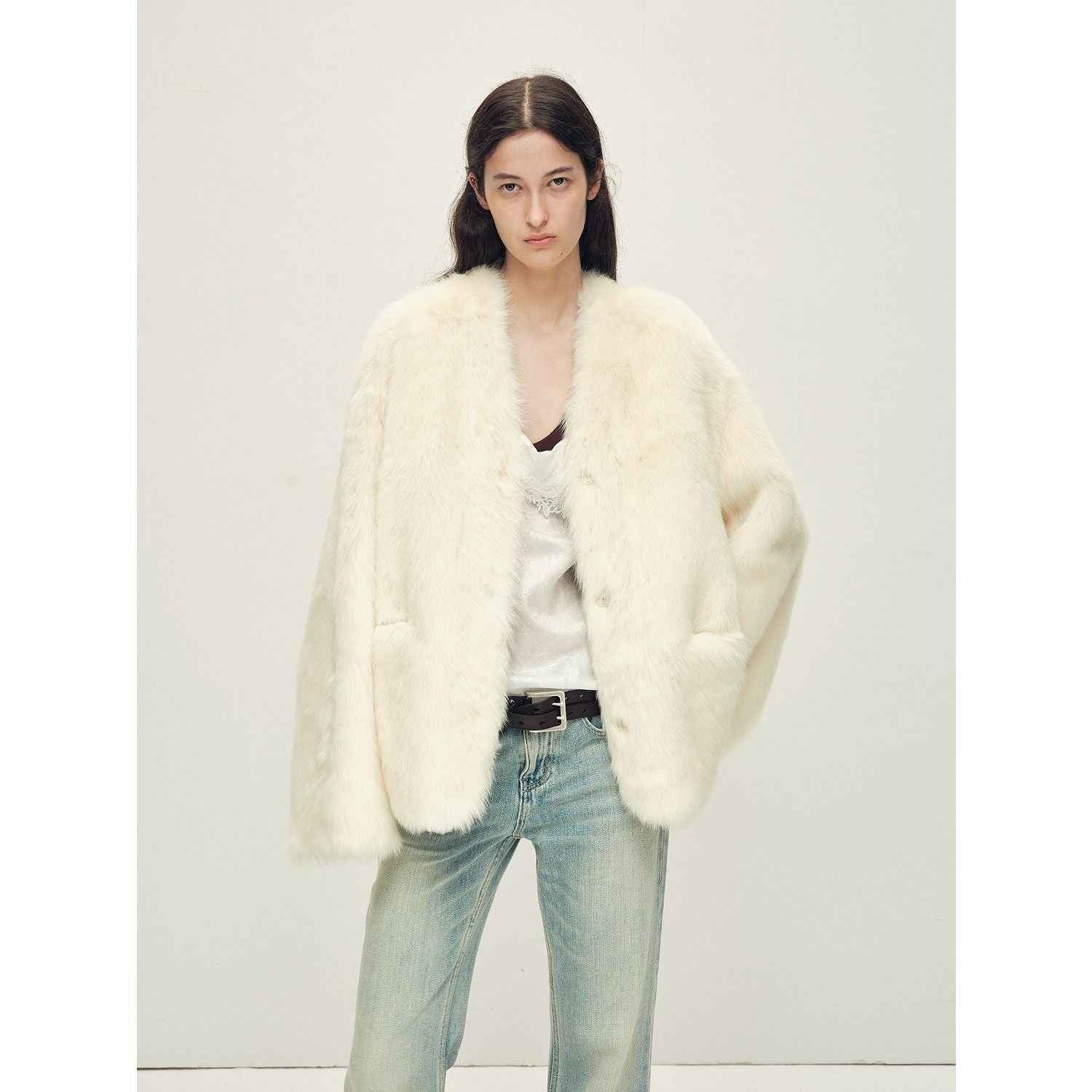 Person wearing a white fur coat over a black top and light blue jeans on a plain background