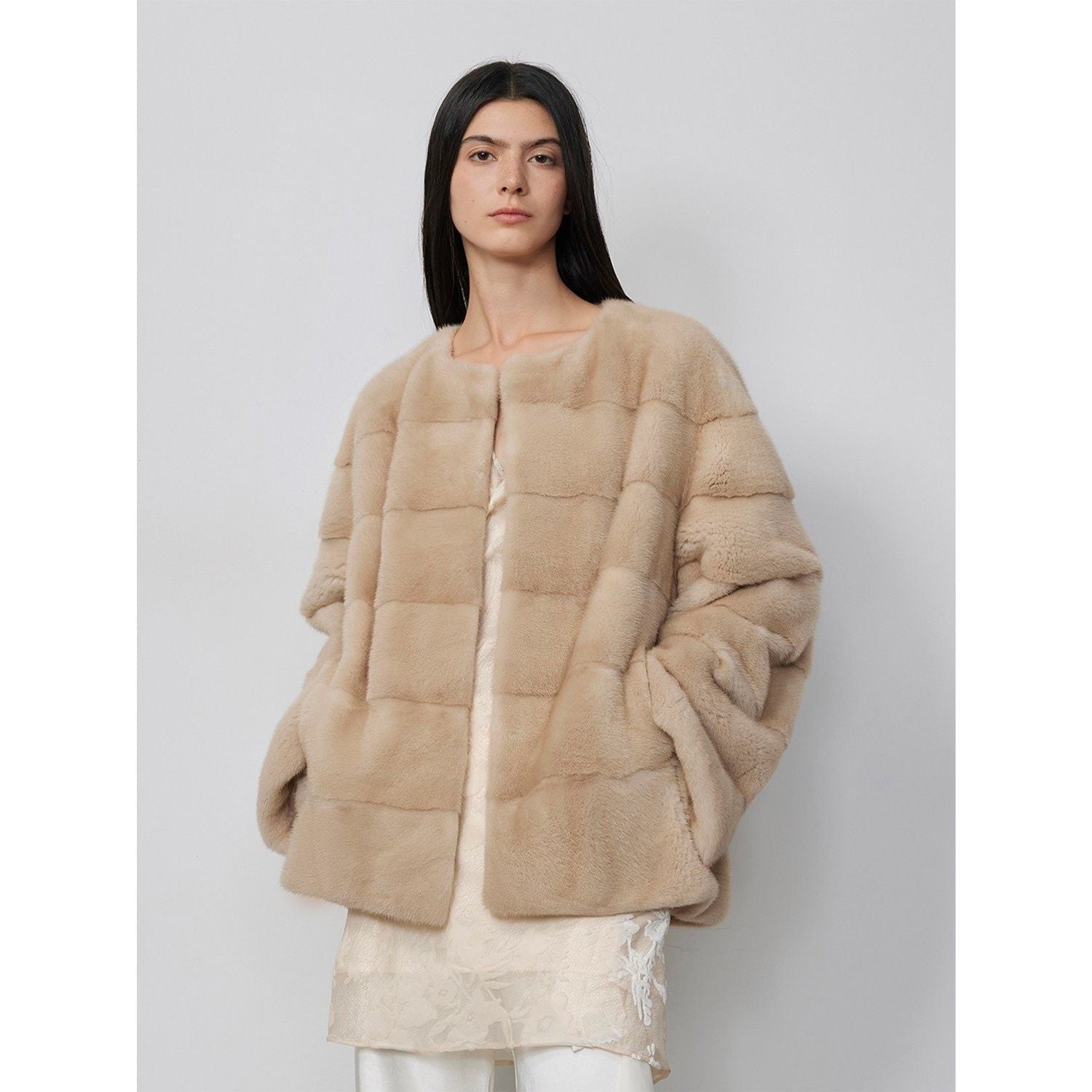Woman wearing a beige fur coat against a plain background