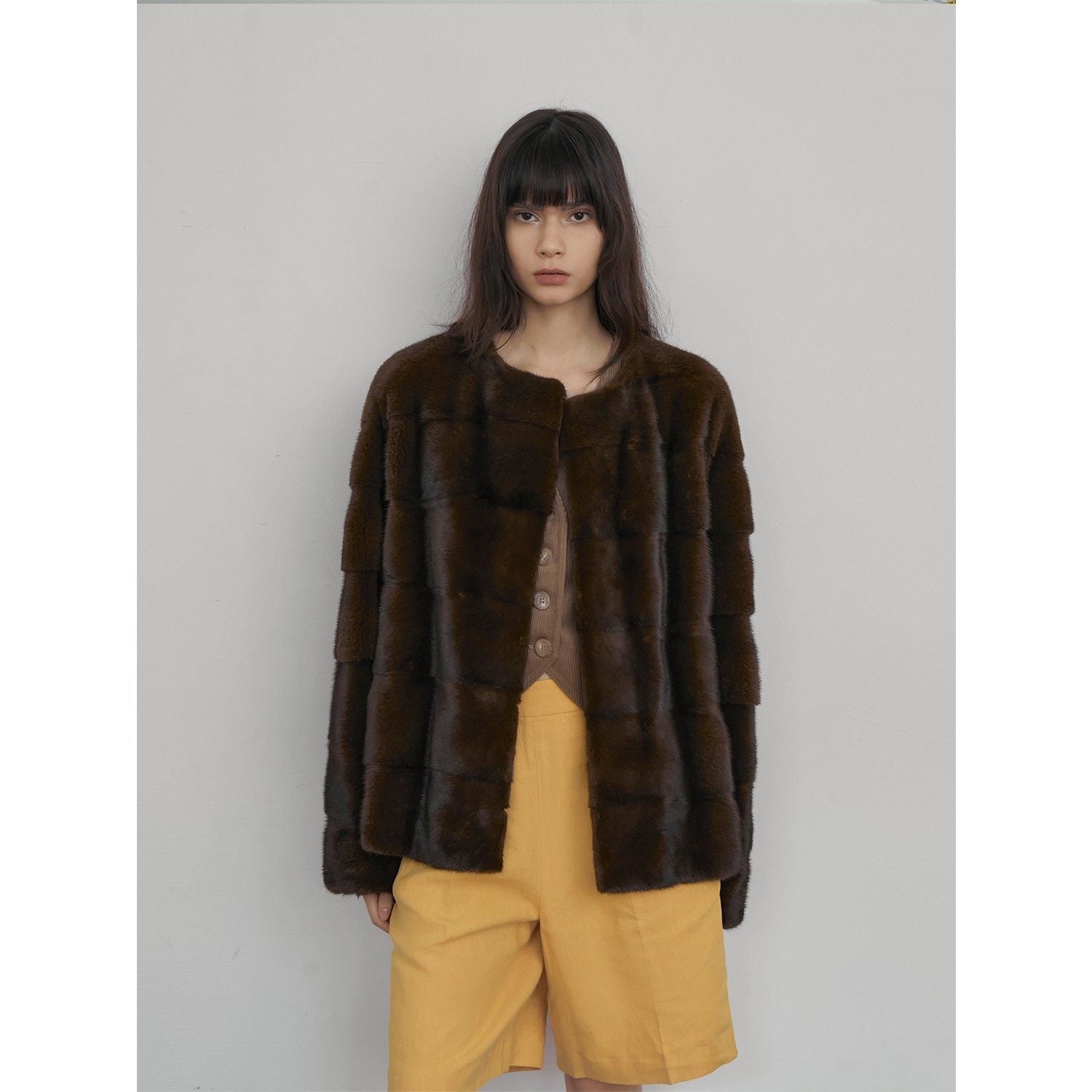 Person wearing a brown fur coat and yellow pants against a plain background