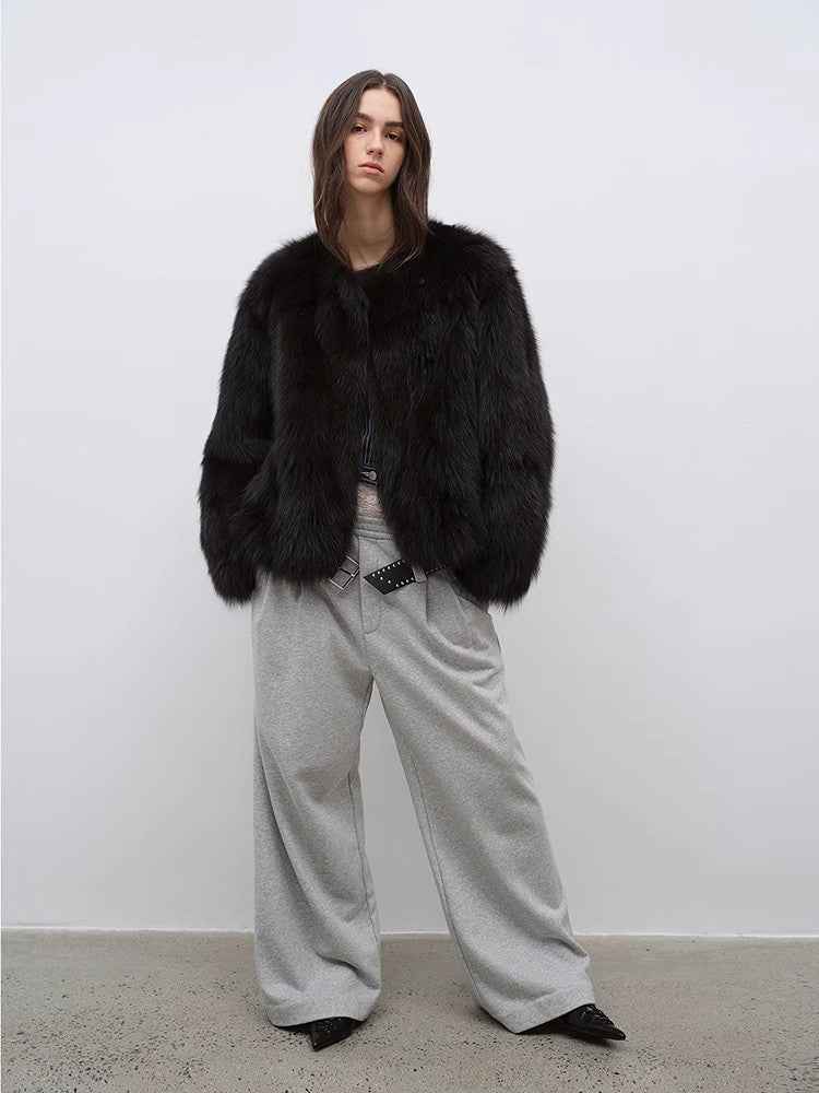 Person wearing a black fur coat and gray pants against a white background