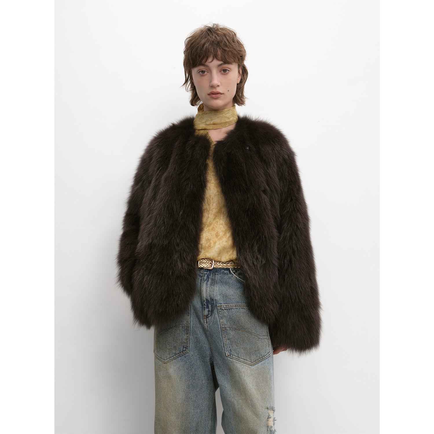 Person wearing a brown fur coat over a yellow sweater and blue jeans on a white background