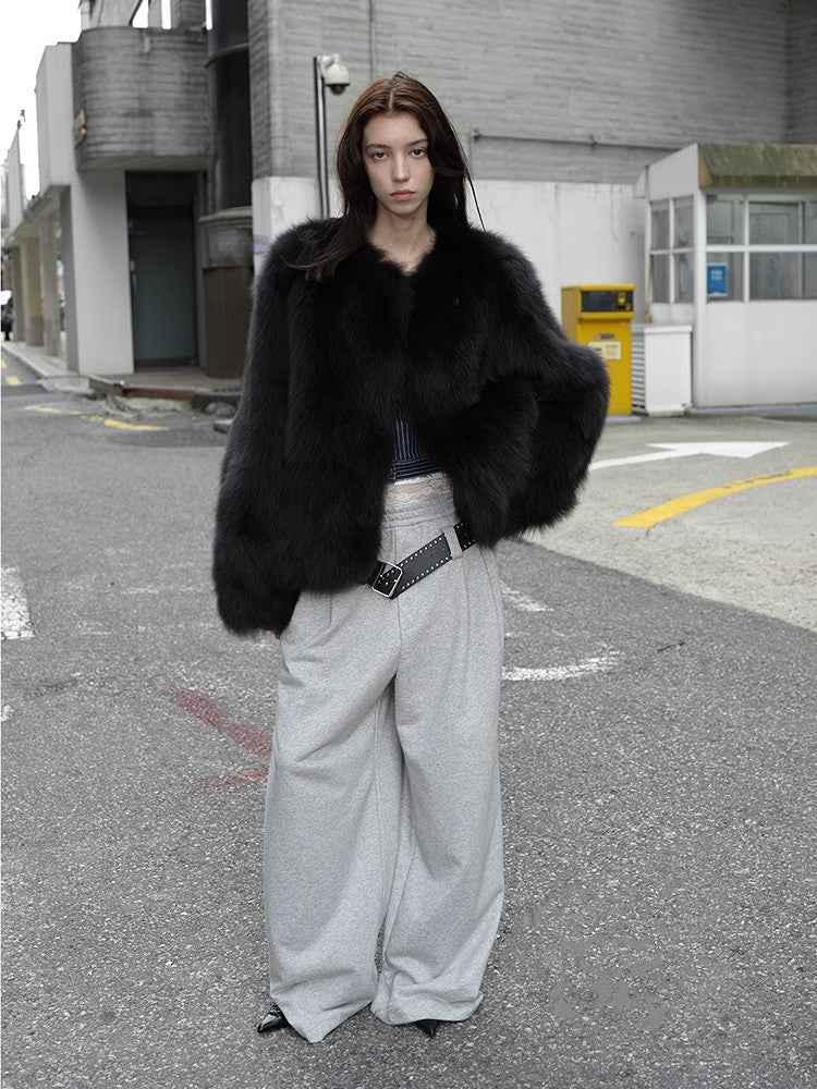 Person wearing a black fur coat and gray pants on an urban street.