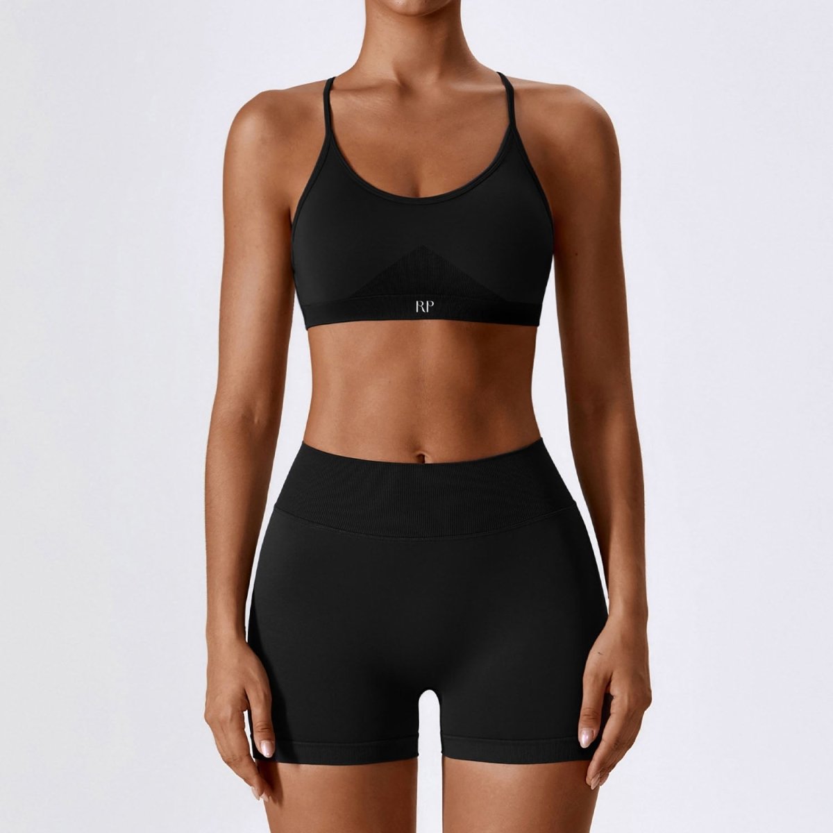 Person wearing a black sports bra and shorts set on a light gray background