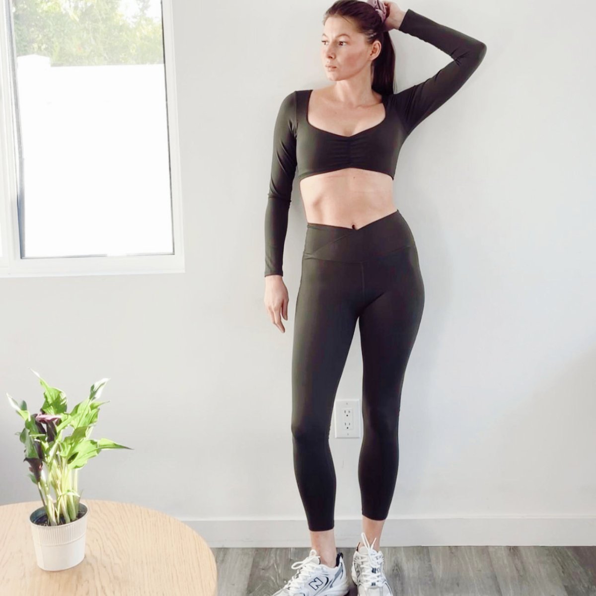 Woman in black athletic wear standing indoors with a plant on a table.