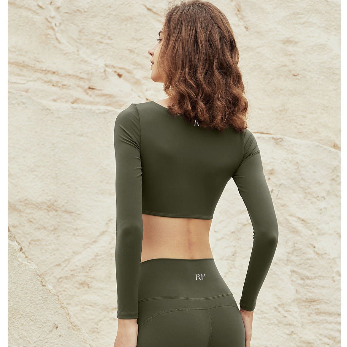 Woman wearing an olive green athletic outfit with a visible brand logo on a beige stone background