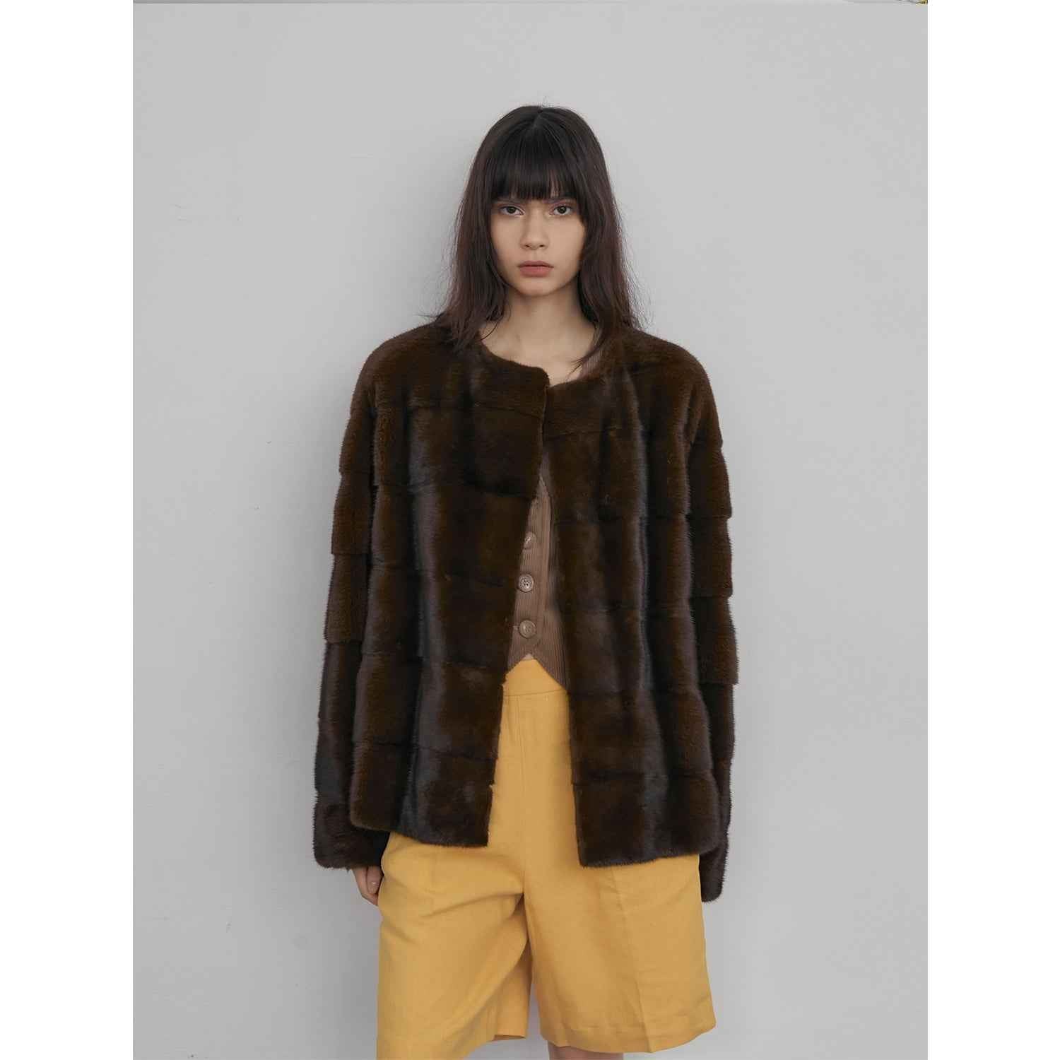 Person wearing a brown fur coat and yellow pants against a plain background