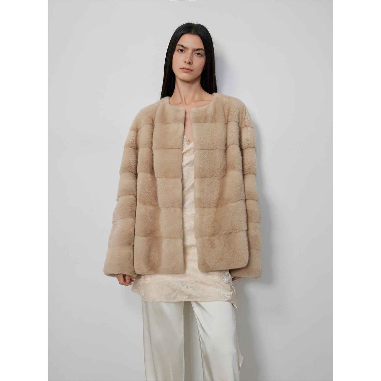 Person wearing a beige fur coat against a plain background