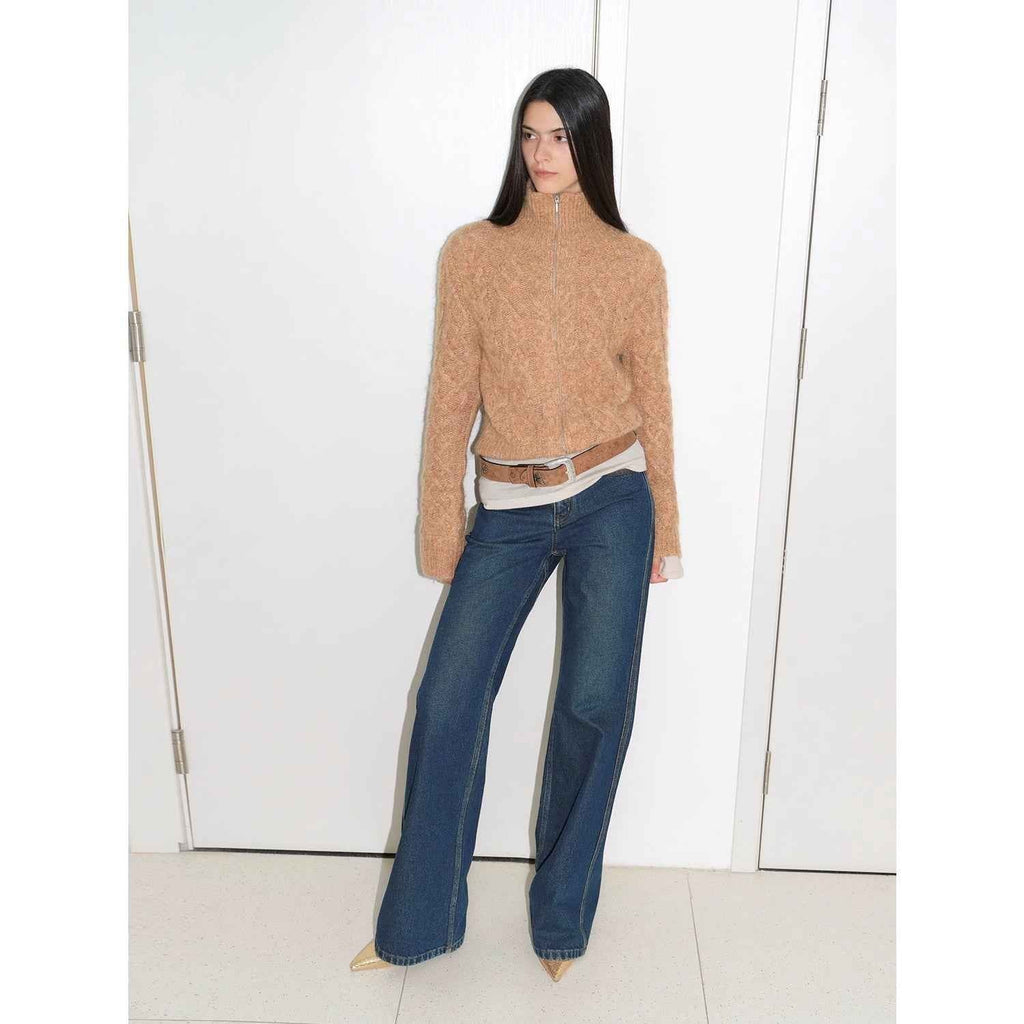 Woman wearing a beige sweater and blue jeans against a white background
